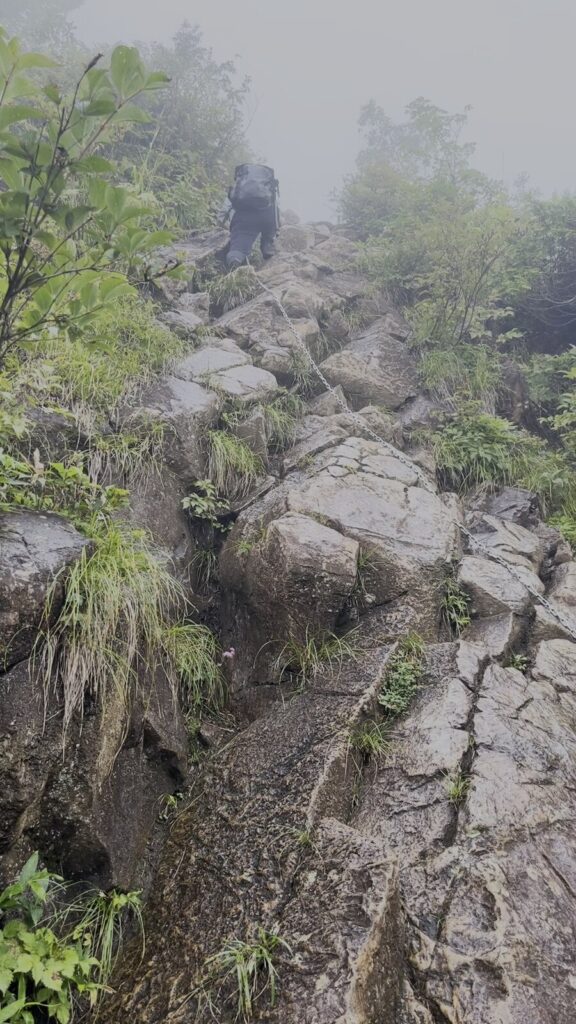 霧の西黒尾根で鎖場を登る同行者の後ろ姿